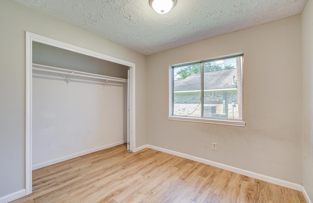 unfurnished bedroom with a textured ceiling, baseboards, wood finished floors, and a closet