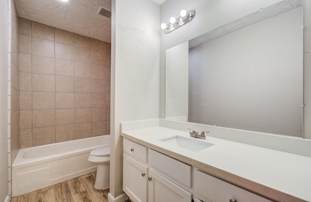 bathroom with vanity, toilet, wood finished floors,  shower combination, and visible vents