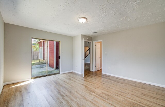 empty room with a textured ceiling, visible vents, stairway, baseboards, and light wood-style flooring
