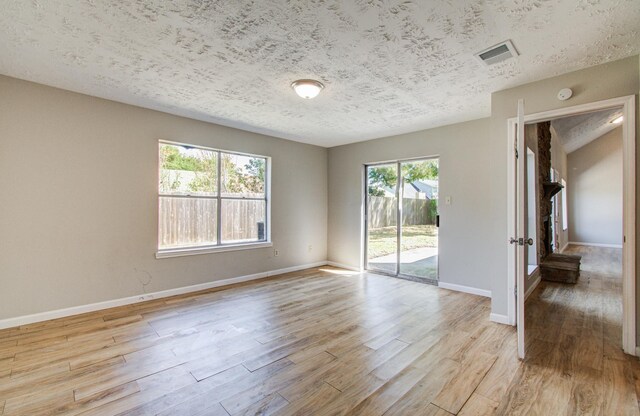unfurnished room with light wood-style floors, baseboards, a textured ceiling, and visible vents