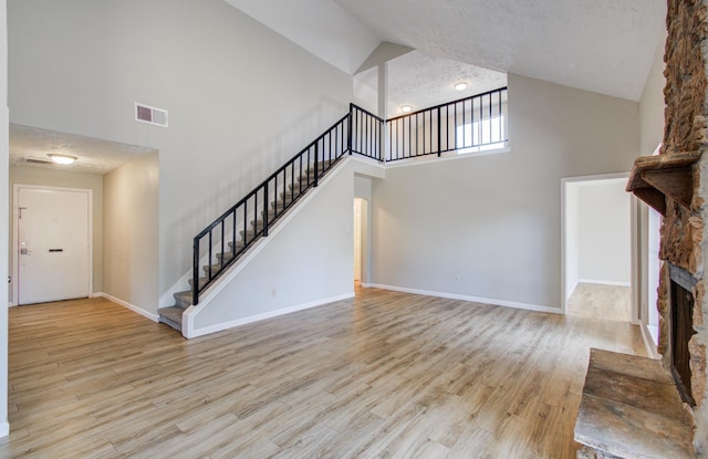 unfurnished living room featuring visible vents, wood finished floors, high vaulted ceiling, and stairway