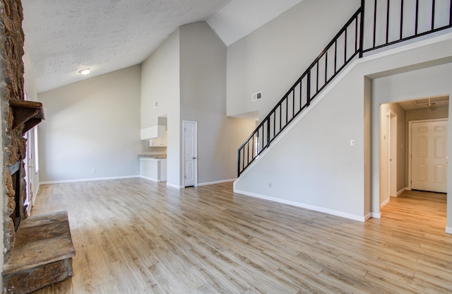 unfurnished living room with visible vents, stairs, baseboards, high vaulted ceiling, and light wood-style flooring