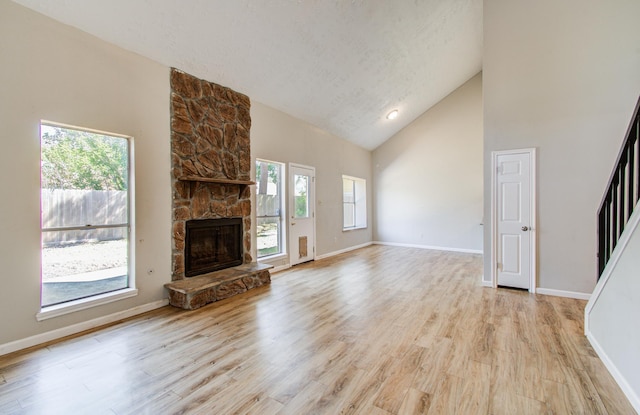 unfurnished living room featuring high vaulted ceiling, a stone fireplace, baseboards, and light wood-style floors