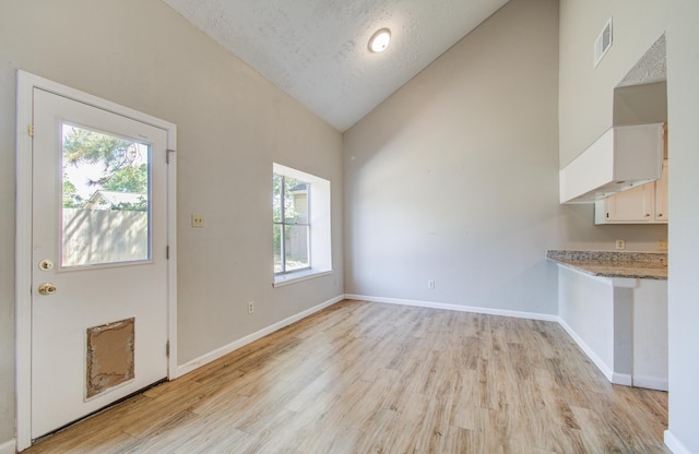 unfurnished dining area featuring visible vents, plenty of natural light, high vaulted ceiling, and light wood-type flooring