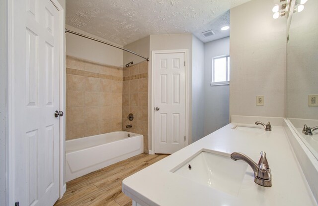 full bath with a sink, visible vents, a textured ceiling, and wood finished floors
