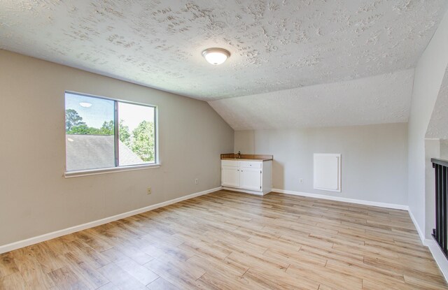 additional living space featuring lofted ceiling, a fireplace, baseboards, a textured ceiling, and light wood finished floors