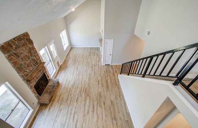 interior space with a high ceiling, a fireplace, baseboards, wood finished floors, and visible vents