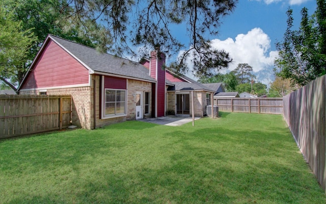 rear view of house with central AC, a fenced backyard, a chimney, brick siding, and a yard