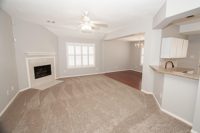 unfurnished living room featuring carpet, ceiling fan with notable chandelier, a tile fireplace, and visible vents