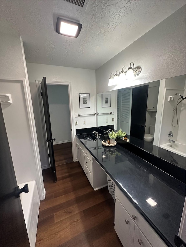 full bathroom featuring a sink, double vanity, toilet, a textured ceiling, and wood finished floors