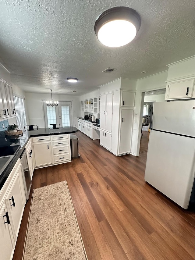 kitchen with dark countertops, a textured ceiling, freestanding refrigerator, stainless steel dishwasher, and visible vents