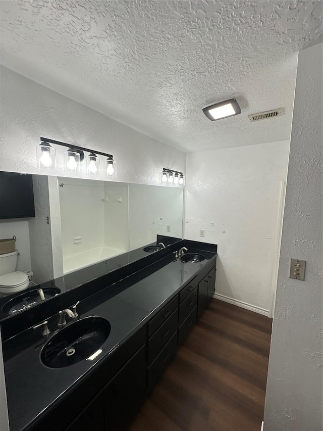 bathroom featuring visible vents, a sink, a textured ceiling, and wood finished floors