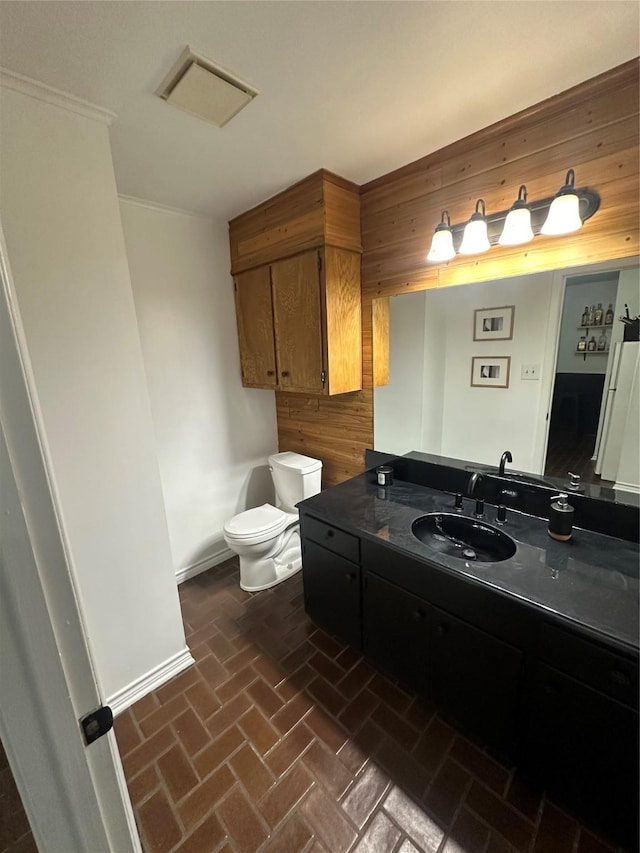 half bathroom featuring brick floor, vanity, toilet, wood walls, and baseboards