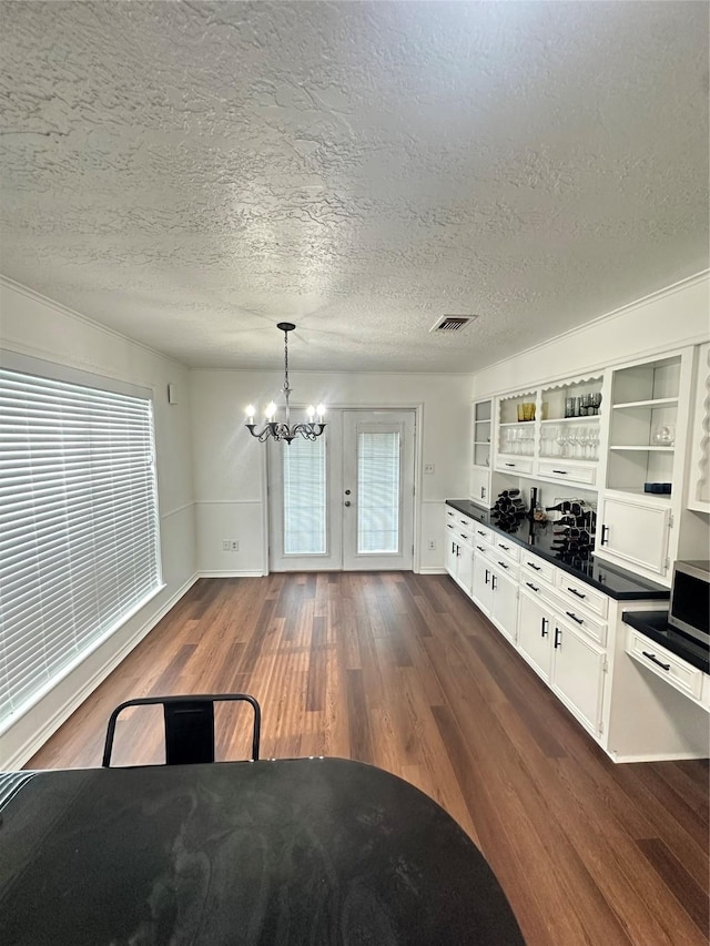 interior space with an inviting chandelier, open shelves, dark countertops, stainless steel microwave, and dark wood finished floors
