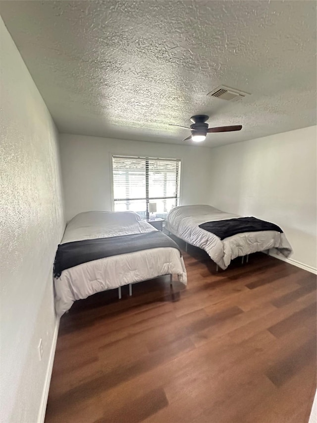 bedroom featuring visible vents, wood finished floors, baseboards, a textured ceiling, and a ceiling fan