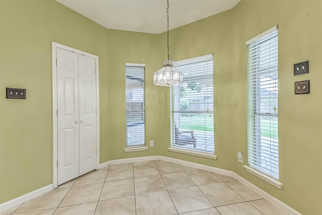 unfurnished dining area featuring light tile patterned flooring, baseboards, and a chandelier