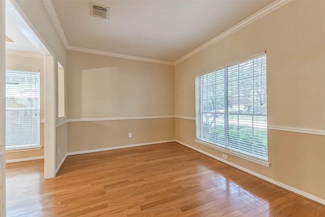 empty room with a healthy amount of sunlight, crown molding, light wood finished floors, and visible vents