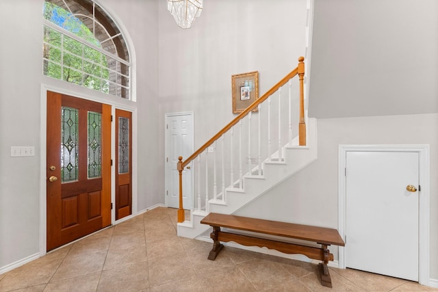 tiled foyer with baseboards, stairs, a chandelier, and a towering ceiling