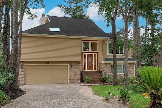 bi-level home featuring brick siding, a chimney, a garage, and aphalt driveway