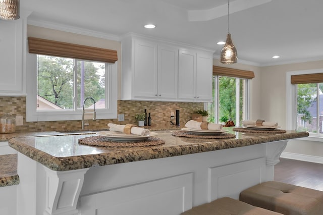 kitchen with a sink, light stone counters, recessed lighting, white cabinetry, and backsplash