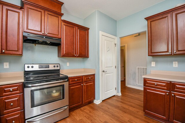 kitchen featuring electric range, visible vents, light wood-type flooring, light countertops, and under cabinet range hood