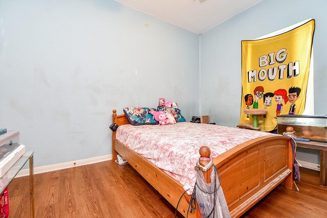 bedroom featuring baseboards, wood finished floors, and vaulted ceiling
