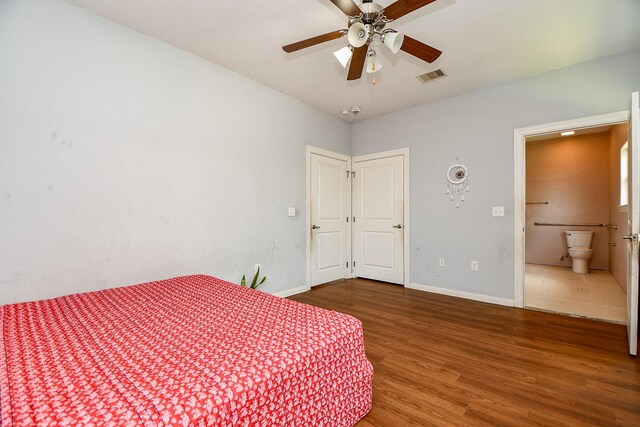 bedroom featuring baseboards, ensuite bath, wood finished floors, and visible vents