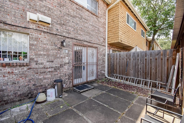view of exterior entry featuring brick siding, a patio area, and fence