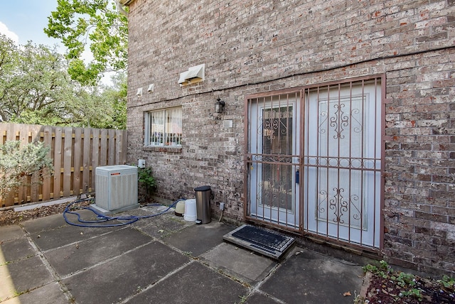 entrance to property featuring brick siding, central AC, and fence