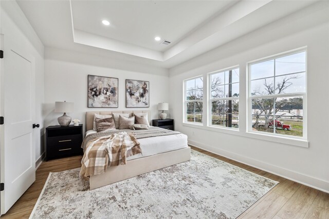 bedroom with multiple windows, a tray ceiling, wood finished floors, and visible vents