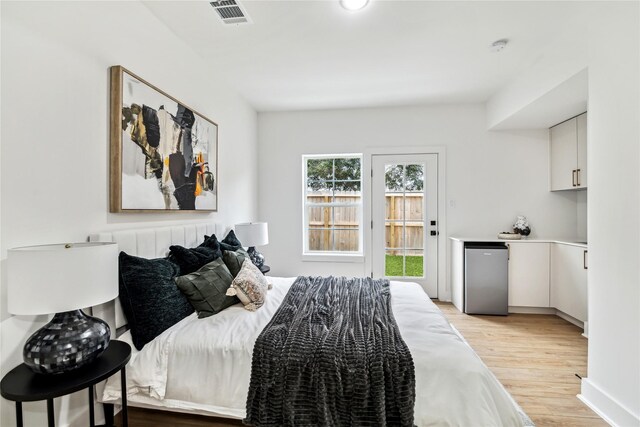 bedroom with access to outside, visible vents, stainless steel fridge, and light wood-style flooring
