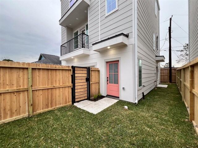 rear view of house featuring a fenced backyard, a gate, a yard, and a balcony