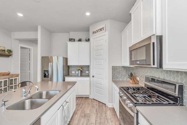 kitchen with a sink, appliances with stainless steel finishes, light wood-style flooring, and white cabinetry