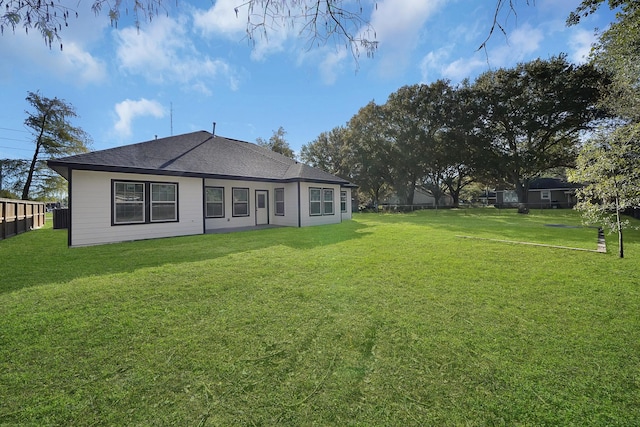 rear view of house featuring fence, a shingled roof, and a yard