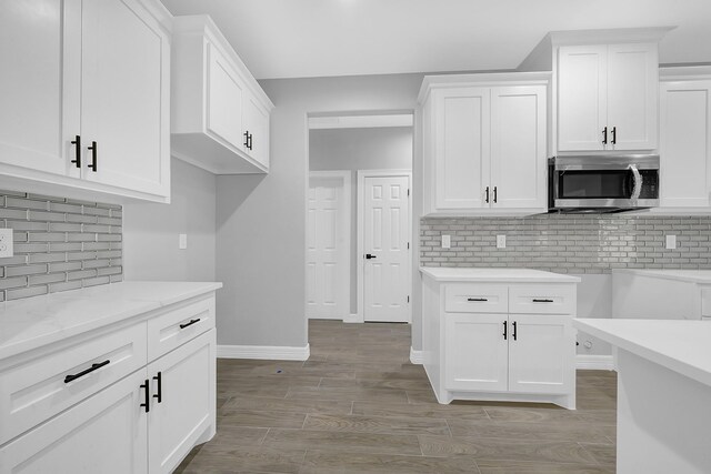 kitchen with white cabinetry, stainless steel microwave, and tasteful backsplash