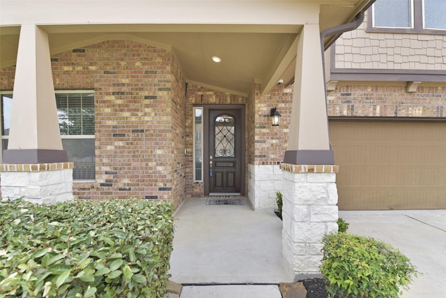 view of exterior entry featuring a garage, a porch, and brick siding