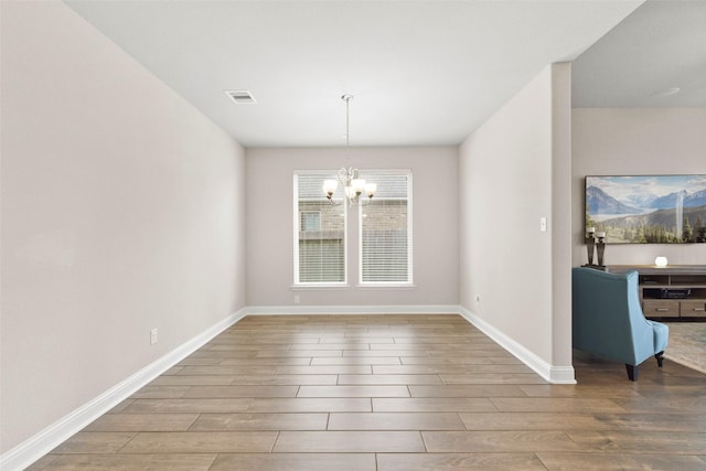 unfurnished dining area with baseboards, an inviting chandelier, wood finished floors, and visible vents