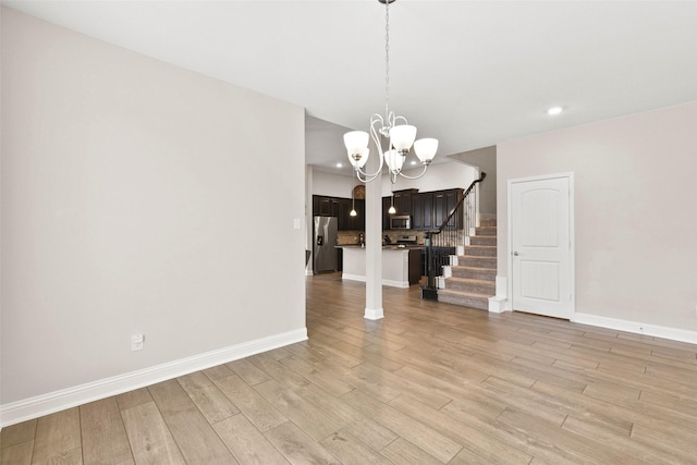 unfurnished dining area with baseboards, light wood finished floors, stairs, and a chandelier