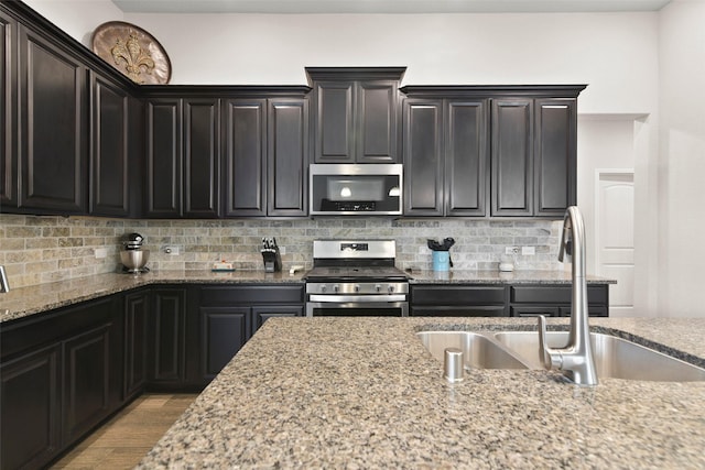 kitchen with light stone countertops, a sink, light wood finished floors, stainless steel appliances, and decorative backsplash