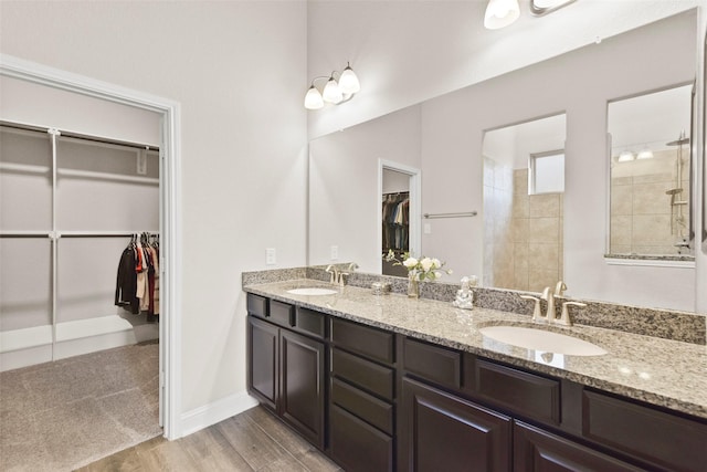 bathroom with a sink, tiled shower, double vanity, and wood finished floors