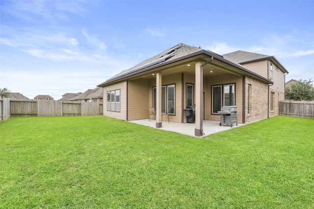 rear view of property with a patio, a fenced backyard, brick siding, roof mounted solar panels, and a lawn