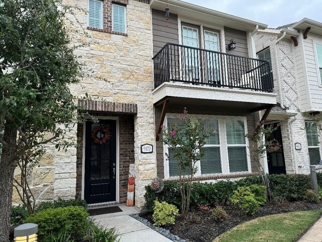 view of exterior entry with a balcony and stone siding