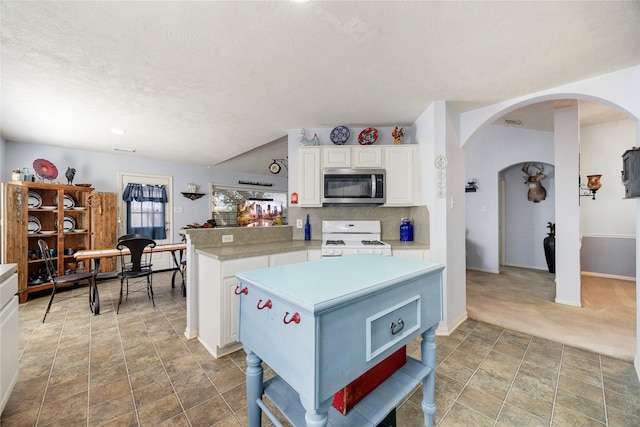 kitchen with white gas stove, arched walkways, light countertops, white cabinets, and stainless steel microwave