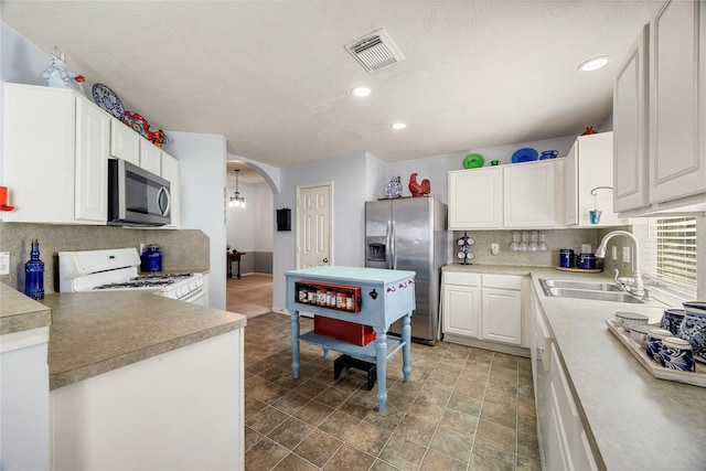 kitchen featuring appliances with stainless steel finishes, a sink, arched walkways, backsplash, and visible vents