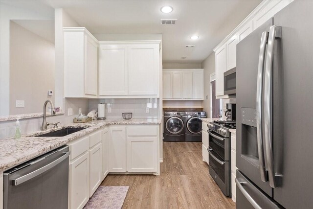 kitchen with light wood-style floors, white cabinetry, a sink, independent washer and dryer, and stainless steel appliances