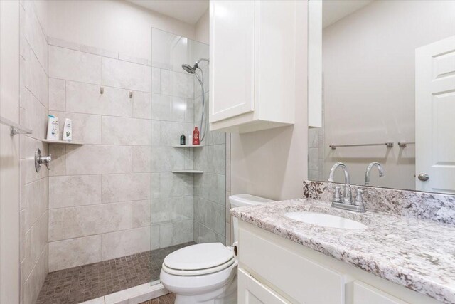 full bathroom with toilet, a tile shower, and vanity