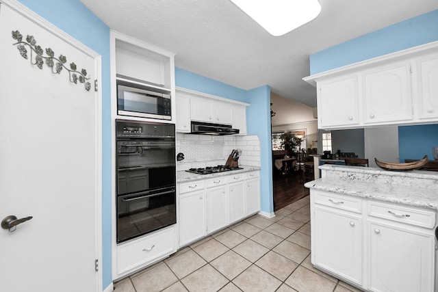kitchen featuring tasteful backsplash, white cabinets, black appliances, under cabinet range hood, and light tile patterned flooring