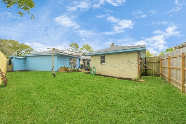 rear view of property with a lawn, brick siding, and fence