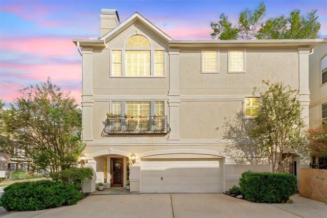 traditional-style home with an attached garage, stucco siding, a chimney, concrete driveway, and a balcony