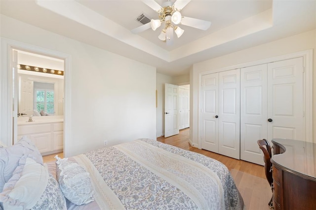 bedroom featuring visible vents, a closet, light wood-type flooring, connected bathroom, and a tray ceiling